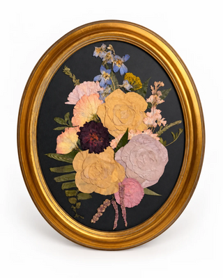 Preserved wedding bouquet in a vintage gold oval frame with a black background.