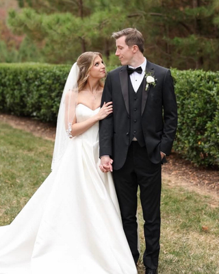 Bride in a strapless white wedding gown and long veil standing outdoors beside the groom in a landscaped garden.