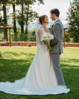 Bride and groom standing together outdoors, holding a white calla lily wedding bouquet.