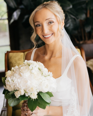 Smiling bride in a white wedding dress holding a classic and timeless bouquet of white roses and greenery.
