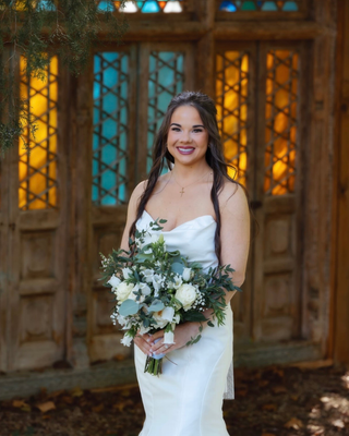 Bride holding a white and green wedding bouquet in front of a wooden doorway.
