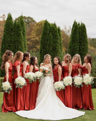 The bride and bridesmaids in burgundy dresses holding white floral bouquets outdoors.