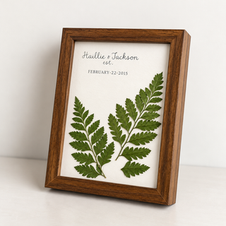Custom wedding keepsake featuring two pressed green fern fronds and personalized names and wedding date in an ivory mat with a walnut wood frame by Forgiven Flower.