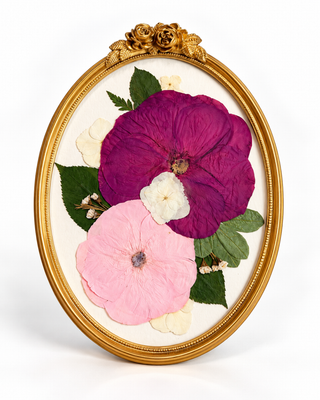 Pressed flowers arranged in a gold, vintage oval frame with white backing.
