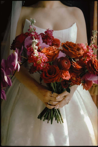 Close-up of a bride holding a dramatic bouquet of red, burgundy, orange, and purple flowers.