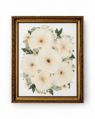 Custom pressed wedding bouquet featuring ivory and white flowers, pale blue blooms, and muted green foliage in an ornate vintage gold frame by Forgiven Flower.