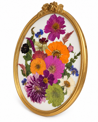 Colorful pink, purple, orange, and yellow pressed flowers arranged in an ornate gold vintage oval frame.