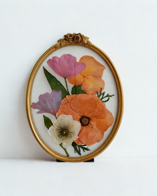 Orange, pink, and purple pressed flowers arranged in an ornate gold vintage oval frame.
