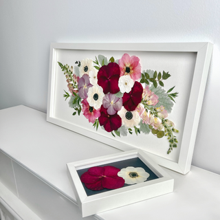 Custom pressed wedding flowers in a white frame with burgundy, blush pink, lavender, and ivory blooms, displayed alongside a smaller floral keepsake frame by Forgiven Flower.