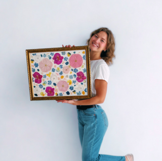 Woman posing with pressed wedding bouquet art arranged in a vintage, antique, gold frame. 