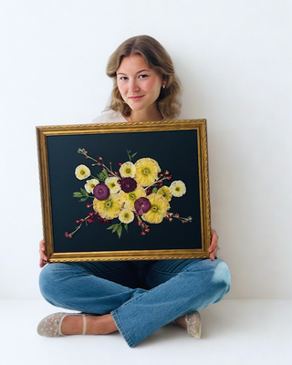 Woman holding pressed flower artwork in a vintage frame with black background 